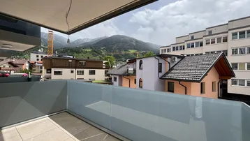 Balkon mit Glasbrüstung und weitem Blick auf die umliegenden Berge und Gebäude.