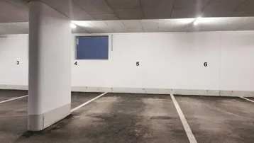 Tiefgarage mit nummerierten Stellplätzen, sauberem Betonboden und einem kleinen Fenster.