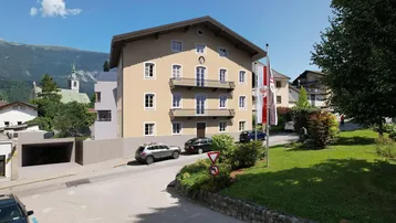 Mehrstöckiges Gebäude mit traditioneller Architektur, Balkonen und Bergblick in einer städtischen Umgebung.