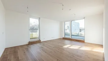 Heller Wohnraum mit Holzboden und großen Fenstern, die Zugang zu einem französischen Balkon bieten.