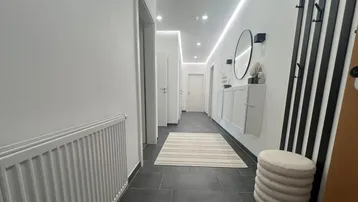 Moderner Flur mit dunklen Fliesen, weißer Wandgarderobe und indirekter Deckenbeleuchtung.