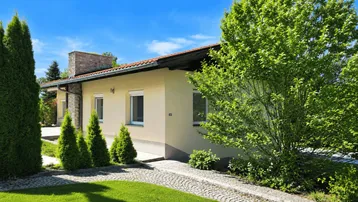 Einfamilienhaus mit heller Fassade, Ziegeldach und gepflegtem Vorgarten unter blauem Himmel.