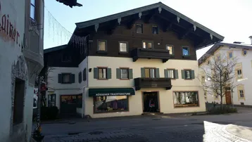 Traditionelles Gebäude mit Holzbalkonen und Fensterläden, gelegen an einer Straße mit Geschäften im Erdgeschoss.