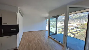 Heller offener Wohnbereich mit integrierter Küche, Parkettboden und Zugang zum Balkon mit Bergblick.