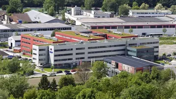Luftaufnahme eines modernen Gebäudekomplexes mit begrünten Dächern und umliegender Vegetation in einer Gewerbezone.