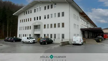 Großes Gewerbegebäude mit vielen Fenstern, Laderampen und Parkplätzen unter bewölktem Himmel.