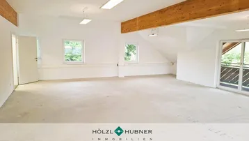 Geräumiger, heller Innenraum mit sichtbaren Holzbalken und großen Fenstern, bereit für den Ausbau.
