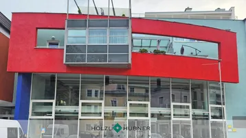 Moderne Geschäftsfassade mit großen Glasflächen und roten Akzenten, die das Stadtbild widerspiegeln.