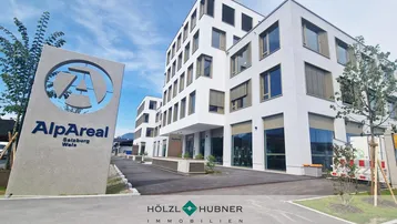 Modernes weißes Bürogebäude mit großen Fenstern und einem prominenten Firmenschild unter blauem Himmel.