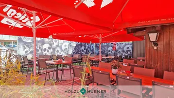Großer Außenbereich mit roten Sonnenschirmen, Tischen und Stühlen, ideal für Gäste.