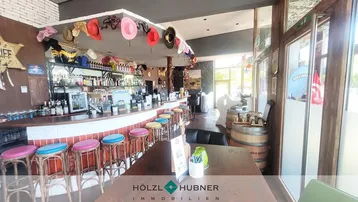 Eine lebhafte Bar mit vielen bunten Hüten als Dekoration und Holzhockern an der Theke.