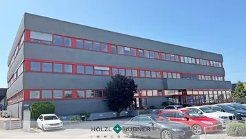 Modernes Bürogebäude mit grauer Fassade und roten Fensterrahmen unter blauem Himmel.