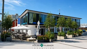 Modernes Geschäftsgebäude mit großen Glasfronten und einem Café mit Außenterrasse im Erdgeschoss.