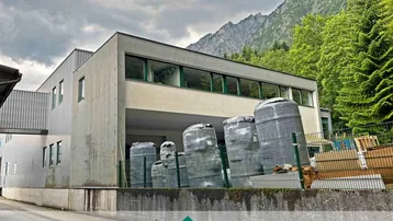 Modernes Industriegebäude mit Lagerbereich und Blick auf die umliegenden Berge unter bewölktem Himmel.