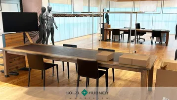 Geräumiger Bürobereich oder Showroom mit Holzboden, großem Konferenztisch und Schaufenstern.