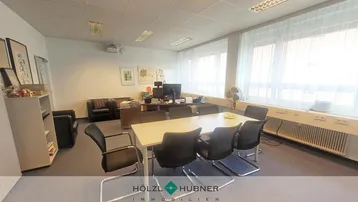 Geräumiges Büro mit Konferenztisch, Teppichboden und großen Fenstern, die viel Tageslicht hereinlassen.