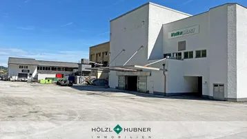 Außenansicht eines Industriegebäudes mit großem Vorplatz unter blauem Himmel.