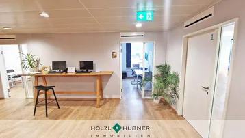 Heller Empfangsbereich mit Holzboden, Arbeitsplätzen und Zugang zu weiteren Büroräumen.