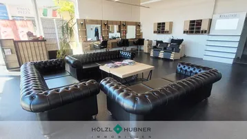 Geräumiger Friseursalon mit modernen Arbeitsplätzen, bequemen Ledersofas und großen Fenstern für viel Tageslicht.