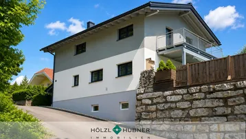 Modernes Einfamilienhaus mit heller Fassade, dunklen Fenstern und einem Balkon im Obergeschoss.