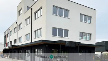 Modernes Geschäftsgebäude mit weißer und dunkelgrauer Fassade und großen Fenstern im Erdgeschoss.