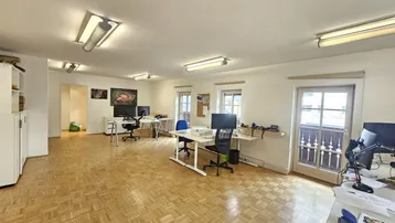Geräumiges Büro mit hellem Parkettboden, mehreren Arbeitsplätzen und Zugang zu einem traditionellen Balkon.