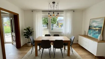 Helles Esszimmer mit Holztisch, modernen Stühlen und Blick ins Grüne durch das Fenster.