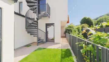 Moderne Außenansicht eines Gebäudes mit schwarzer Wendeltreppe und kleiner Rasenfläche.