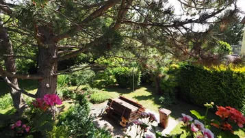 Blick vom Balkon in den grünen Garten mit Bäumen und einer Sitzgelegenheit.