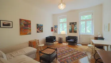 Helles Wohn- und Esszimmer mit Parkettboden, Kunstwerken und großen Fenstern.