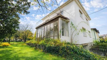Seitenansicht des Hauses mit Wintergarten, großem Rasenbereich und üppiger Vegetation.