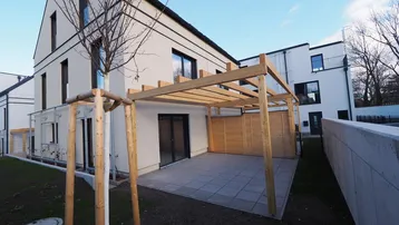 Moderne Terrasse mit Holzpergola und Sichtschutz, angrenzend an ein neues Wohngebäude.
