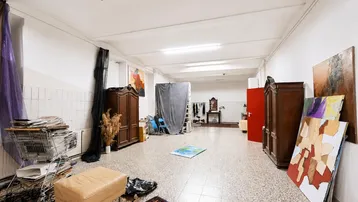 Großer, vielseitiger Raum mit Terrazzoboden, Kunstwerken und verschiedenen Möbelstücken, ideal als Atelier oder Werkstatt.