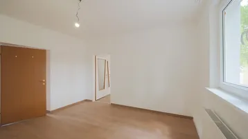 Helles Zimmer mit Parkettboden, weißen Wänden und Blick ins Grüne durch das Fenster.