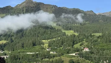 Panoramablick auf die umliegende Berglandschaft mit dichten Wäldern und vereinzelten Häusern.