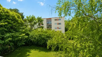 Blick auf ein Mehrfamilienhaus mit grüner Umgebung und Rasenfläche unter blauem Himmel.