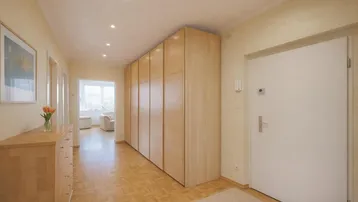 Heller Flur mit Einbauschränken und Parkettboden, der zu einem Wohnbereich führt.