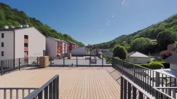 Große Dachterrasse mit Holzboden, Metallgeländer und weitem Blick auf die grüne Umgebung.