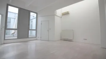 Heller, leerer Raum mit großen Fenstern, hohen Decken und Klimaanlage, ideal für Büronutzung.