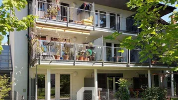 Mehrfamilienhaus mit mehreren Balkonen, die zum Garten hin ausgerichtet sind und viel Grün bieten.
