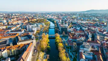Panoramablick aus der Vogelperspektive auf eine Stadt mit Fluss, umgeben von Gebäuden und grünen Ufern.