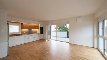 Heller offener Wohn- und Essbereich mit moderner Einbauküche und Zugang zum Balkon.