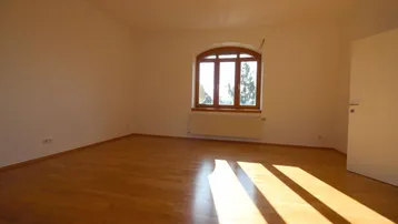 Helles Zimmer mit Holzboden und einem charmanten Rundbogenfenster, durch das Sonnenlicht einfällt.