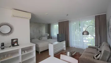 Heller Wohn- und Schlafbereich mit zwei Betten, Sofa, Esstisch und Zugang zum Balkon.