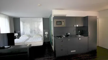 Moderne Studio-Wohnung mit Schlafbereich und integrierter Küchenzeile in dunklen Farbtönen.