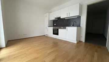 Heller Raum mit integrierter weißer Küchenzeile und warmem Holzparkettboden, ideal für offenes Wohnen.