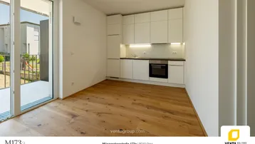 Heller offener Wohnbereich mit integrierter weißer Küche und Zugang zu einem Außenbereich.