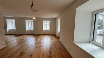 Geräumiger, heller Wohnbereich mit neu verlegtem Holzboden und mehreren Fenstern, bereit zur Einrichtung.