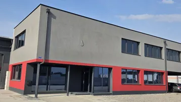 Modernes Geschäftsgebäude mit grauer Fassade, roten Akzenten und großen Fenstern sowie überdachtem Parkplatz.