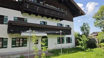 Traditionelles Haus mit Holzbalkonen, grünen Fensterläden und gepflegtem Vorgarten.